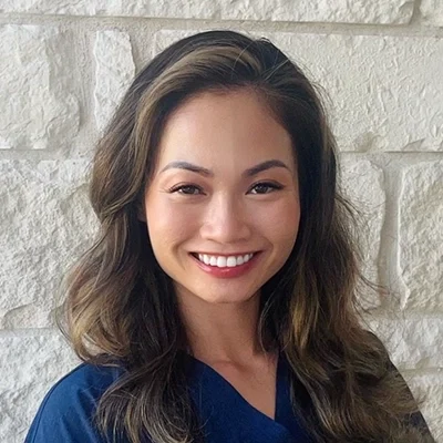 An My Huynh smiling in front of a stone wall.